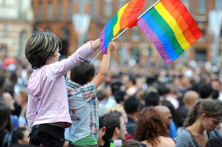 two children waving LGBTQ+ flags in a crowd