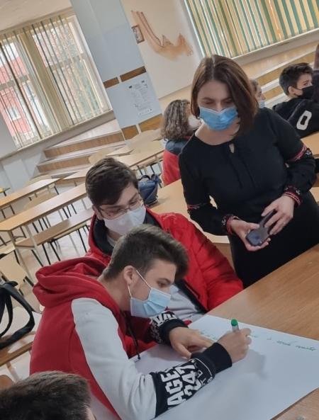 A person in a mask is writing on a poster, while two people watch next to them in masks