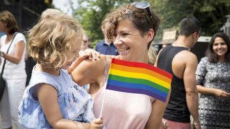A woman holds a little girl in her arms, who is holding an LGBTQ flag.