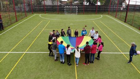 Children holding a round, rainbow blanket on a field